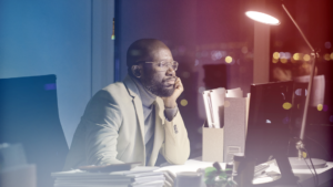 A frustrated business owner leans over his desk, working late into the night.